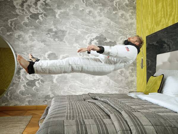 Ein Mann schwebt in einem Raumanzug über einem Bett.