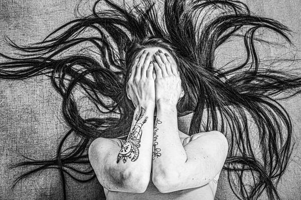Eine Frau hält sich die Hände vor's Gesicht. Ihre sehr langen Haare winden sich wie Schlangen in alle Richtungen. Schwarz-Weiß.