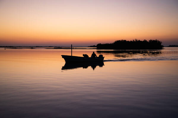 Zwei Menschen in einem motorgetriebenen Boot in einer ruhe ausstrahlenden Abendstimmung.