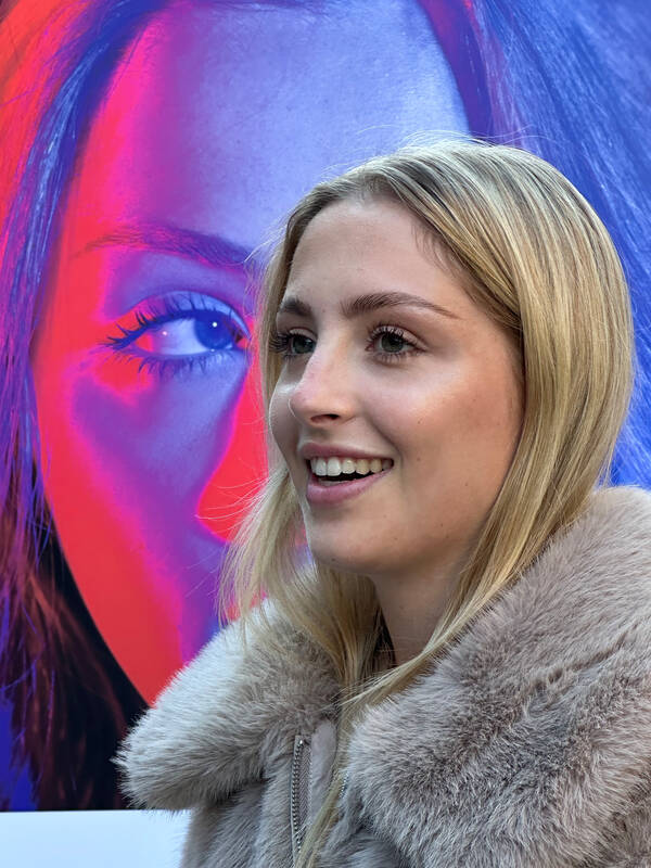 Portrait einer Frau in Pelzmantel vor einem knallig bunt beleuchteten Portrait einer Frau.
