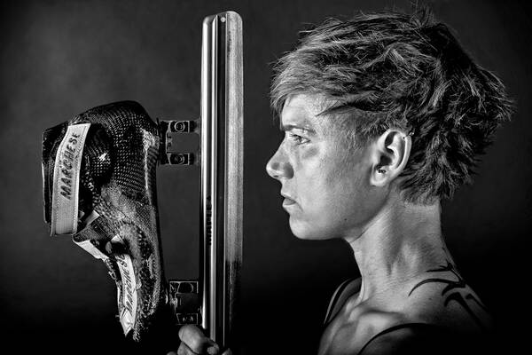 Eine junge, kurzhaarige Frau im Profil hält einen Eisschnelllaufschuh vor ihrem Gesicht. Schwarz-Weiß