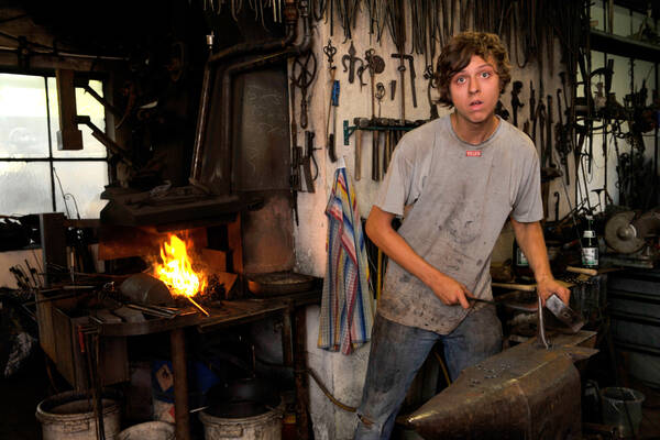 Ein junger Mann an einem Amboss in einer historischen Schmiede.