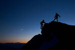 Silhouette zweier Bergsteiger gegen den abendlichen Himmel. Einer sichert von oben den nachkommenden an einem Seil.