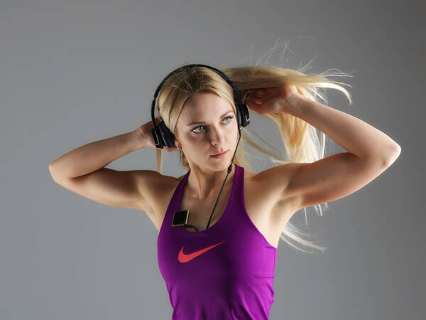 Junge, blonde Frau mit Kopfhörern im Sportoutfit richtet sich die Haare.