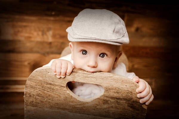 Ein kleinkind mit Mütze steht auf einem Holzsessel und beißt in die Lehne.