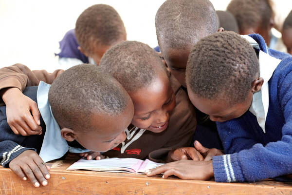 Dunkelhäutige Kinder in blauen Schuluniformen, die sich über ein Buch beugen.