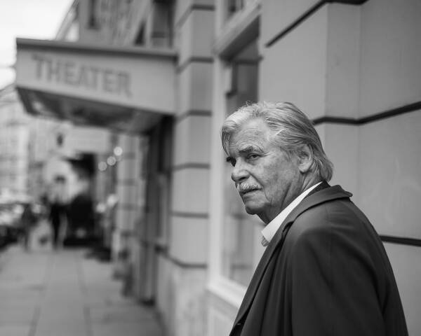 Der Burgschauspieler Peter Simonischek vor dem Eingang eines Theaters. Schwarz-Weiß.