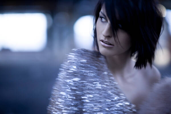 Eine elegant geschminkte, dunkelhaarige Frau in einem asymetrisch geschnittenen Paillettenkleid. Bewegungsunschärfe.