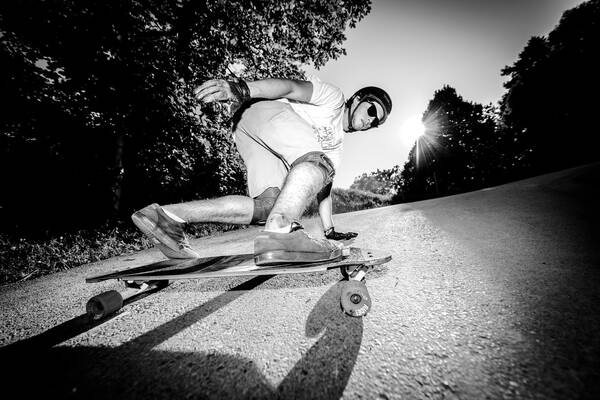 Skateboarder aus tiefer Perspektive fotografiert. die tiefstehende Sonne malt lange Schatten auf den Asphalt. Schwarz-Weiß.