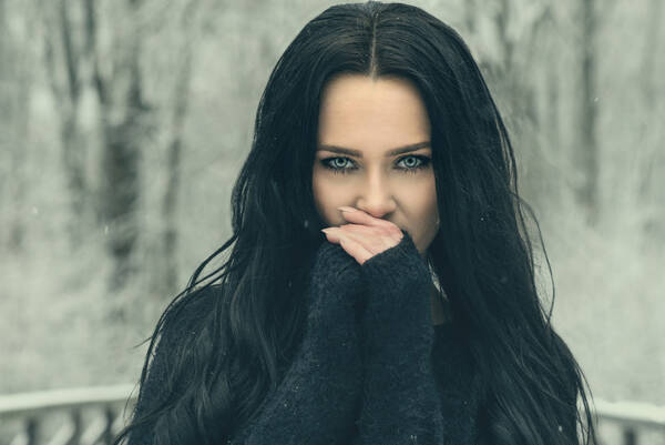 Portrait einer jungen Frau mit schwarzen langen Haaren und schwarzem Pullover auf einer Brücke in einer verschneiten Aulandschaft