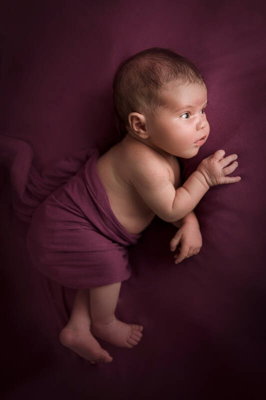 Ein Baby liegt in ein violettes Tuch gewickelt auf einer violetten Unterlage.