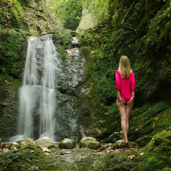 Rückenansicht einer Frau in rotem Oberteil vor einem Wasserfall.