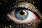 Nahaufnahme eines Auges, das rundum dunkel und mit Glitter geschminkt ist. Die Iris ist auffällig blau und gelb gefärbt.