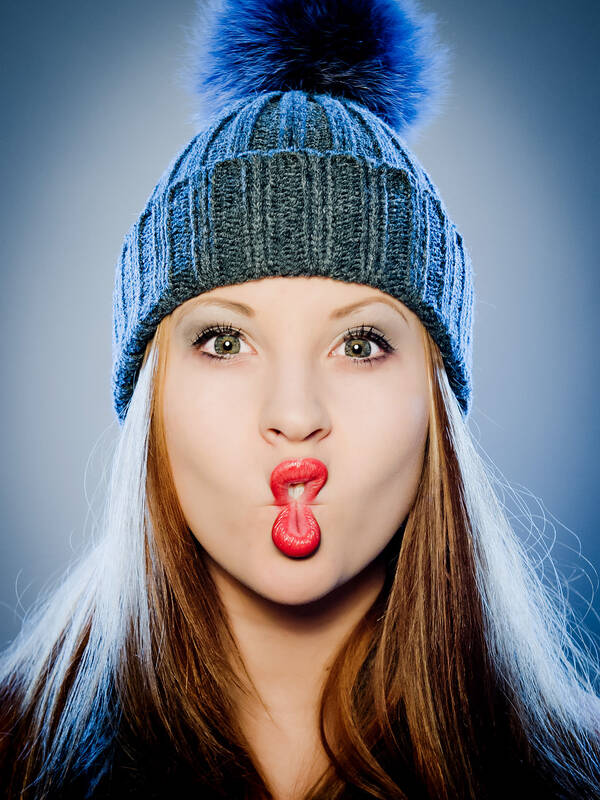 Portrait einer junen Frau mit langen Haaren und einer Strickhaube mit großem Bommel. Sie hat die Wangenflächen so eingesogen, dass die Lippen eine acht formen.