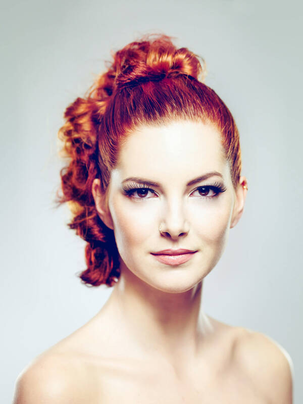 Portrait einer rothaarigen Frau, die lockigen Haare sind nach hinten gebunden. Die Schultern sind unbekleidet.