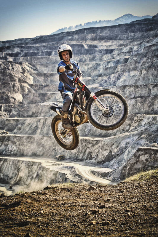 Bild eines Motocross-Fahrers der mit seiner Maschine gerade im Sprung ist. Im Hintergrund die vom Bergbau geschaffenen Hangstufen des steirischen Erzberges.