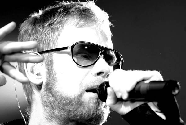 Portrait des Sängers Mark Forster mit Sonnenbrille beim Singen in der Stadthalle Graz mit Mikrophon. Schwarz-Weiß.
