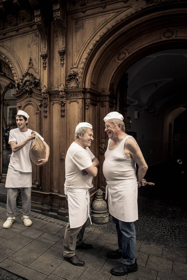 Bäcker stehen in weißen Leibchen und mit weißen Arbeitsschürzen mit Nudelwalker und Mehlsack vor der Hofbäckerei edegger-tax in Graz.