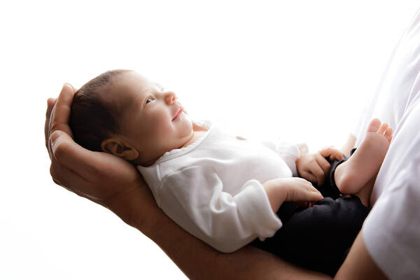 Ein Babie wird von zwei Händen gehalten und lacht.