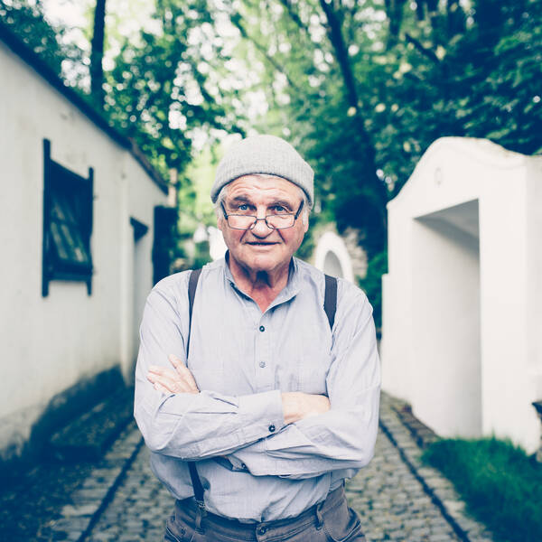 Portrait des österreichischen Autors Peter Turrini in einer Kellergasse mit verschränkten Armen und grauer Wollmütze.