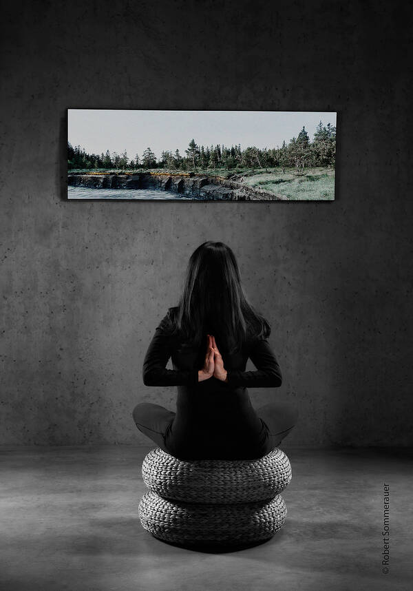 Eine Frau sitzt im Yogasitz mit hinter dem Rücken gefalteten Händen auf zwei übereinandergestapelten grauen Sitzkissen in einem betongrauen Raum und schaut auf ein Panoramabild einer unberührten Uferlandschaft.