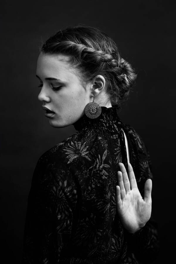 Portrait einer jungen Frau mit Flechtfrisur und elegantem, dunklem Kleid, eine Hant auf dem Rücken. Schwarz-Weiß.