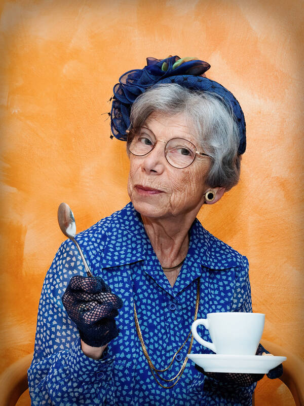 Eine alte Dame in blauem Kostüm mit blauem Hut sitzt mit Kaffeetasse in der linken Hand. In der rechten Hand hält sie den erhobenen Kaffeelöffel.