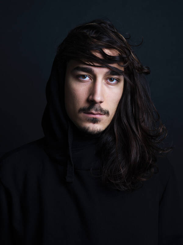 Portrait eines jungen Mannes mit langen Haaren und Bart vor schwarzem Hintergrund