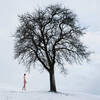 Ein nackter Mann im Schnee unter einem Baum.