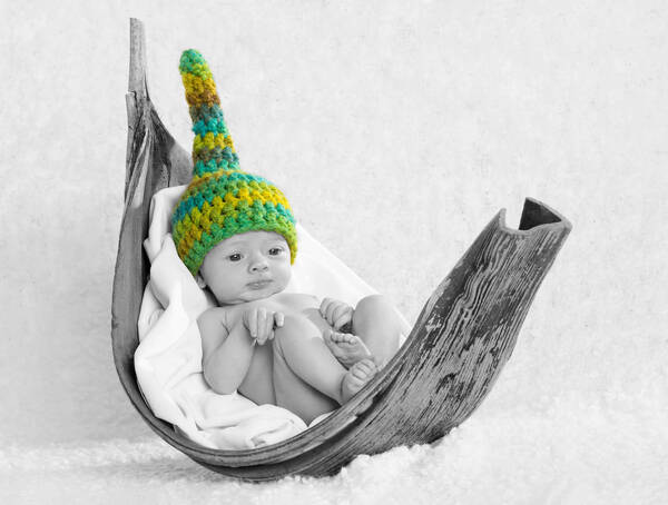 Colour-Key: Ein nur mit einer gehäkelten Mütze bekleidetes Baby liegt in der getrockneten Schale einer großen Frucht. Nur die Mütze ist in verschiedenen Grüntönen färbig, der Rest ist Schwarz-Weiß.