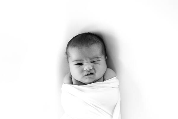 Newborn Baby eingewickelt in Windeln blinzelt ins Licht. Schwarz-Weiß.