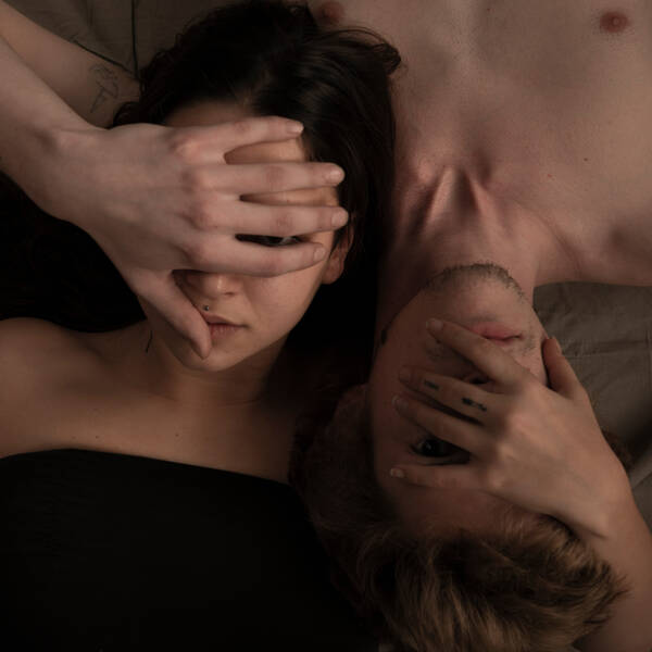 Eine junge Frau und eine junger Mann liegen so, dass ihre Köpfe auf der linken Schulter des jeweils anderen Liegt. Sie bedecken gegenseitig mit der linken Hand das Gesicht.mit 