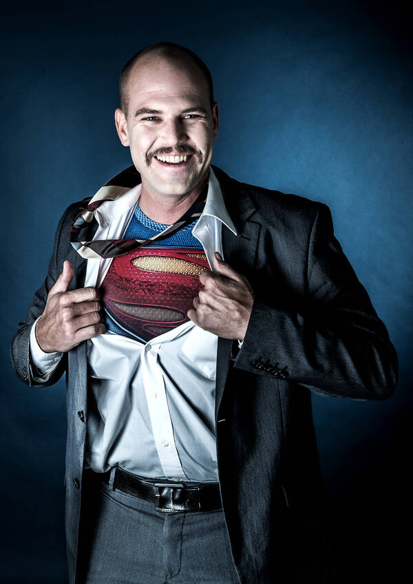 Ein Mann reißt sich das Anzugshemd auf und darunter erscheint das Superman-Kostüm.