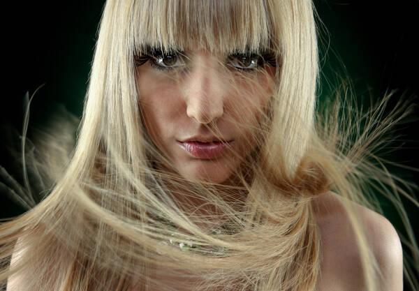 Frau mit langen blonden, sehr geradelinigen Haaren. Wind wirbelt ihre Haare durcheinander.