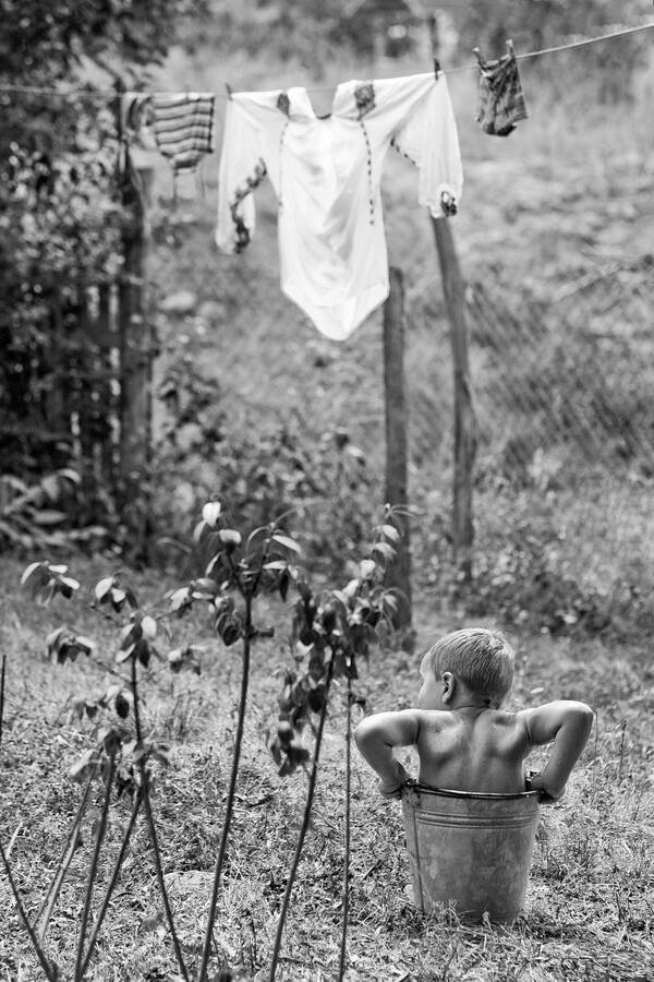 Ein Kind sitzt in einem Eimer unter einer Wäscheleine. Schwarz-Weiß.