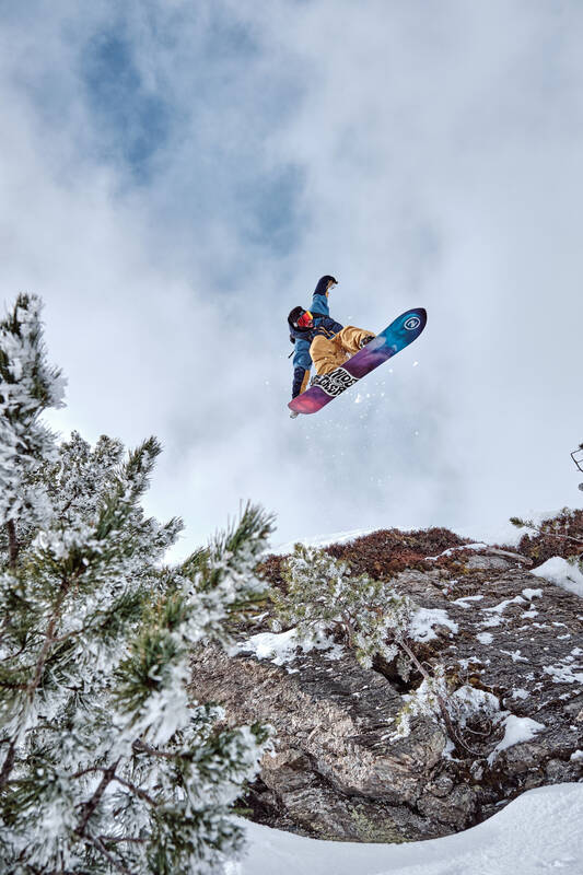 Ein Snowboarder im Sprung über einen Felsen gegen einen bewölkten Himmel fotografiert.