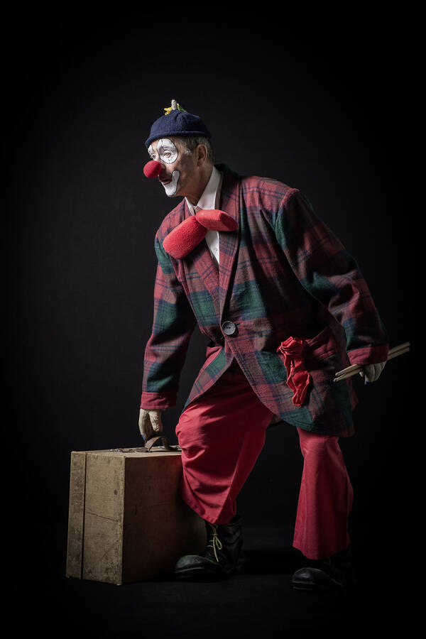 Ein Clown mit trommelstöcken und einem alten Koffer.