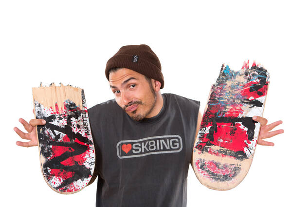 Ein junger Mann mit Mütze hält die Teile eines zerbrochenen Skateboards in die höhe.