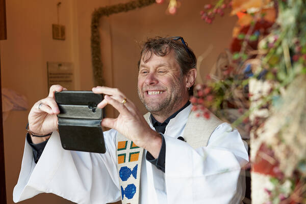 Ein lachender Prister im Ornat macht ein Foto mit dem Mobiltelefon.
