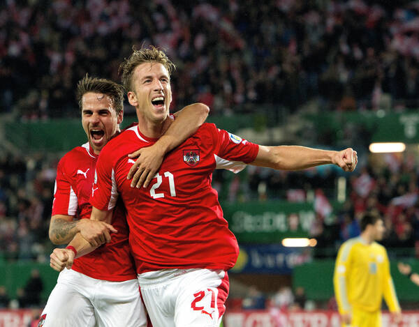 Zwei Fußballspieler in Rot-Weißen Dressen umarmen sich in einem Stadion.