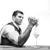 Der Jungwinzer Florian Dillinger presst Trauben in seiner Hand – der Wein daraus fließt sprudelnd in ein Weinglas. Schwarz-Weiß.