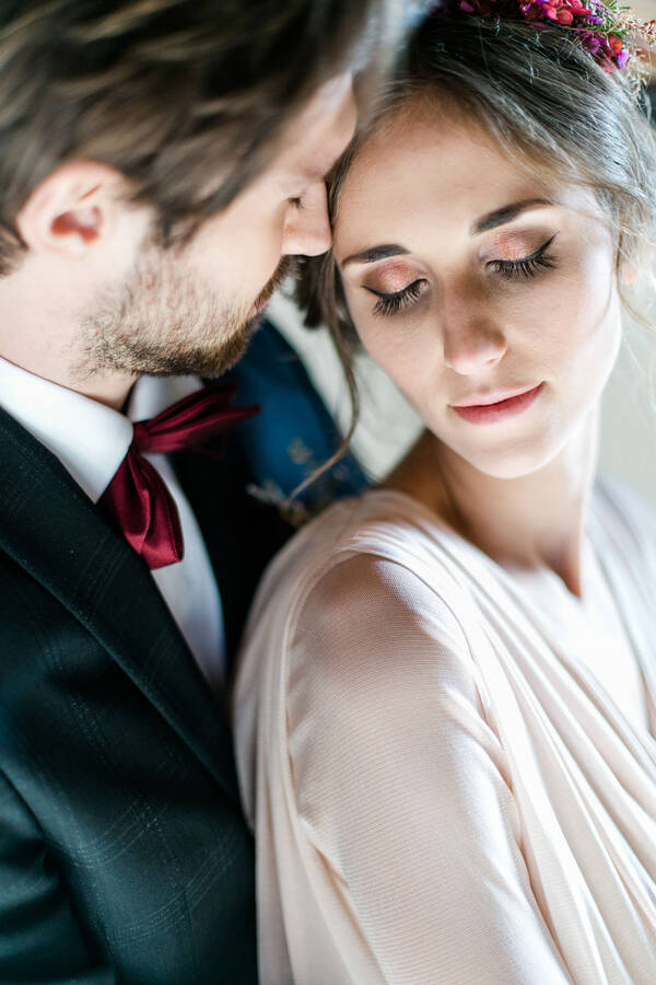 Ein Brautpaar im Close-Up. Der Bräutigam steht hinter der Braut, sie hat den Kopf zur Seite geneigt, seine Nase berührt ihre Schläfe. Beide haben die Augen geschlossen.