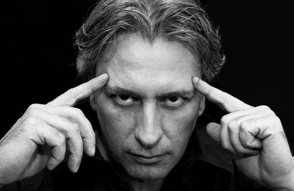 Nahaufnahme eines Mannes, der sich mit beiden Zeigefingern an die Stirn tippt. Schwarz-Weiß.