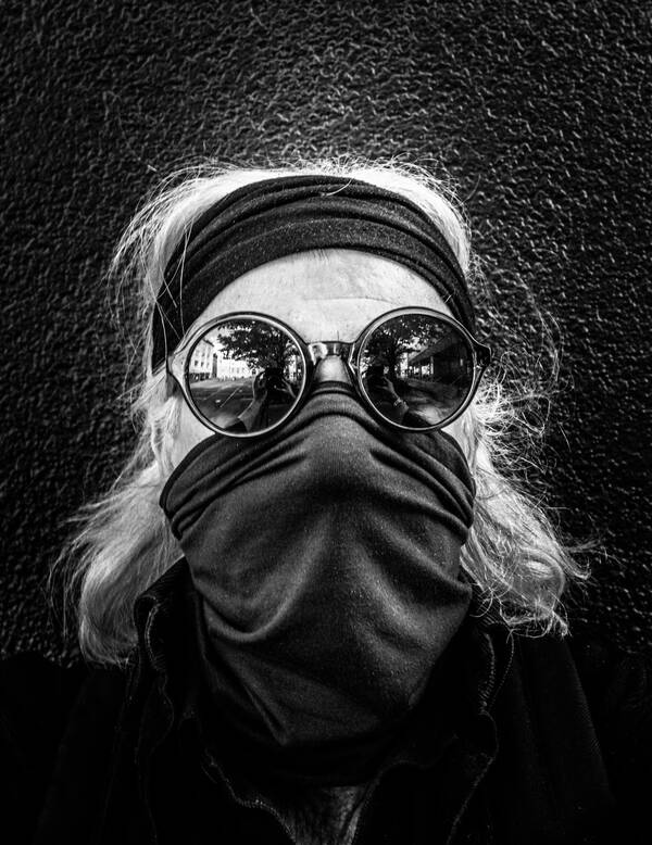 Portrait eines Mannnes mit Sonnenbrille und Stirnband. Ein Tuch verhüllt Mund und Nase als Covid19-Schutz. Schwarz-Weiß.