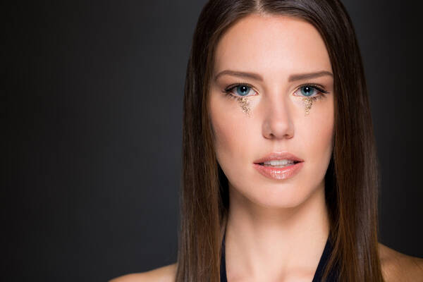Portrait einer jungen Frau mit glatten langen Haaren und Glitter unter den Augen.