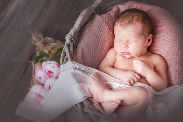 Ein Baby schläft in einem Körbchen mit einer weißen Decke zugedeckt.