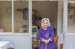 Eine alte Frau steht mit einem Stock in der Türe, durchs Fenster sieht man eine Uhr