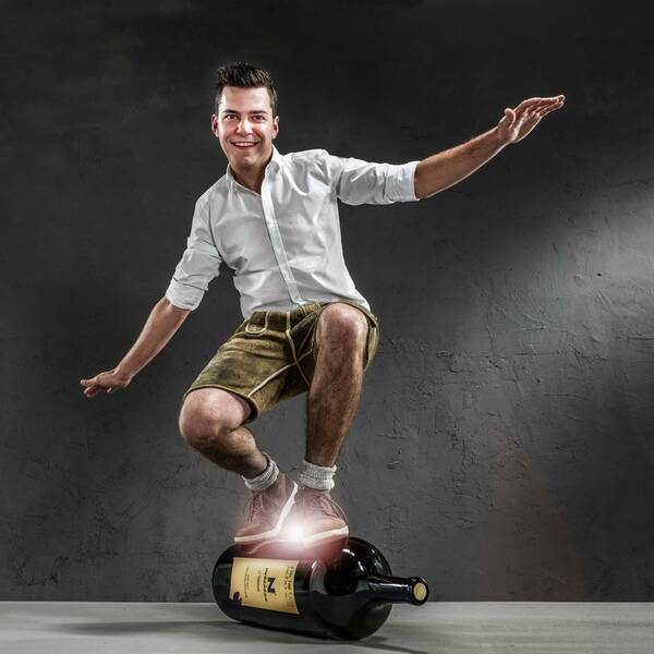 Der Weinbauer Johannes Pichler-Schober steht in Surfer-Pose auf einer Magnum-Weinflasche.
