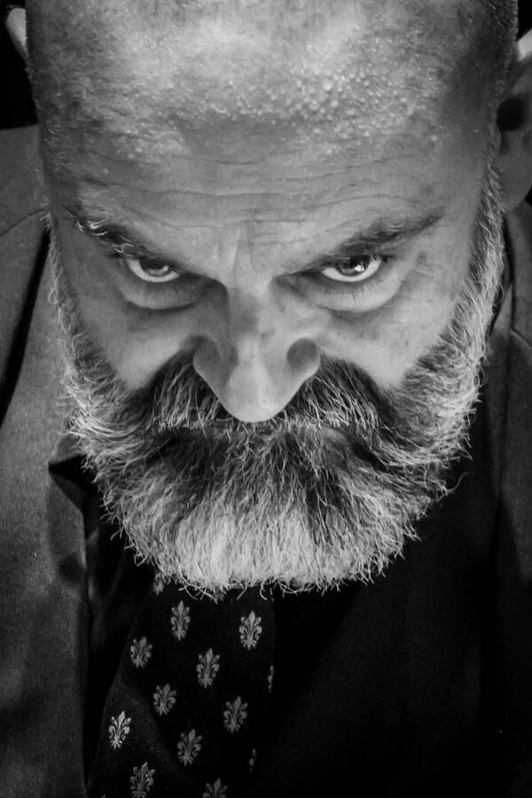 Ein bärtiger Mann mit Schweißtropfen auf der Stirn blickt von unten in die Kamera. Schwarz-Weiß.