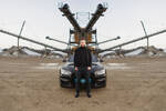 Foto von einem Mann, der zentral im Bild vor einem Auto steht, im Hintergrund diverse Industrieanlagen. Das gesamte Bild ist bis auf den Mann in der Mittenachse horizontal gespiegelt.